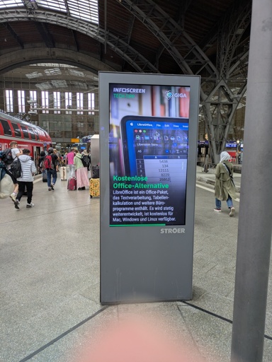 Ein Foto von einer digitalen Werbetafel auf einem Bahnsteig. Die Werbetafel zeigt "Kostenlose Office-Alternative" und maacht Werbung für LibreOffice.